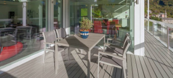 Überdachte Terrasse mit grauem Holzboden, modernem Esstisch-Set und Blick in den offenen Wohnbereich.