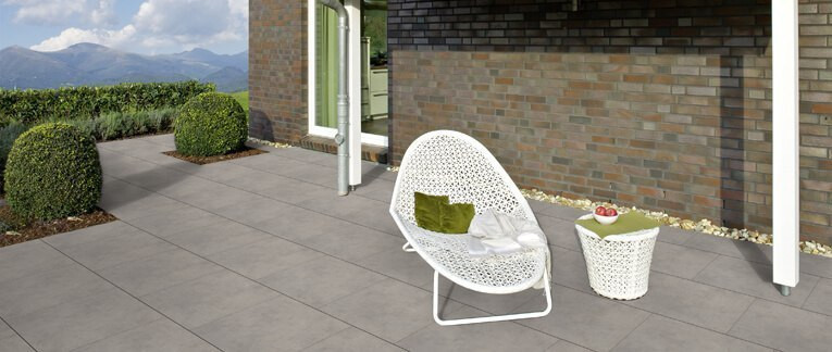 Moderne Terrasse mit großen grauen Fliesen, weißem Loungesessel, Beistelltisch und Blick auf die Berge.